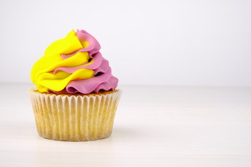 Cupcake with yellow and purple cream on on white wooden table.