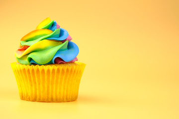Cupcake with rainbow colorful cream on yellow background.