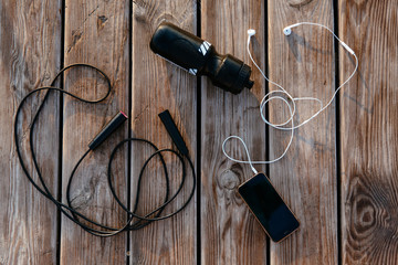 View from top on mobile phone with earphones, jump rope and bottle of water against the wood background. Sport concept.
