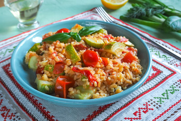 Bulgur with vegetables in a plate on a green kitchen table.