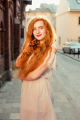 Naklejka premium Smiling ginger model with long hair wearing white dress with naked shoulders