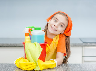 Happy little girl with cleaning supplies in bucket at kitchen