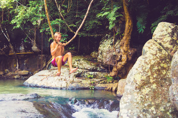 Fototapeta na wymiar Man laughing and having fun while hanging on liana in the jungle.