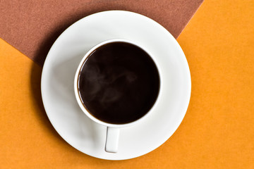 Top view of cup hot black coffee on an orange and brown surface