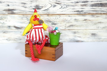 Soft handmade rooster cock toy in red shorts and red stripes in white dot paws sits on wooden box