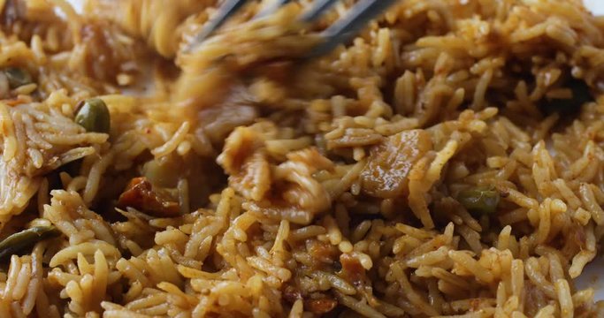 Close view of using a fork to get a forkful of spicy rice on a white plate.