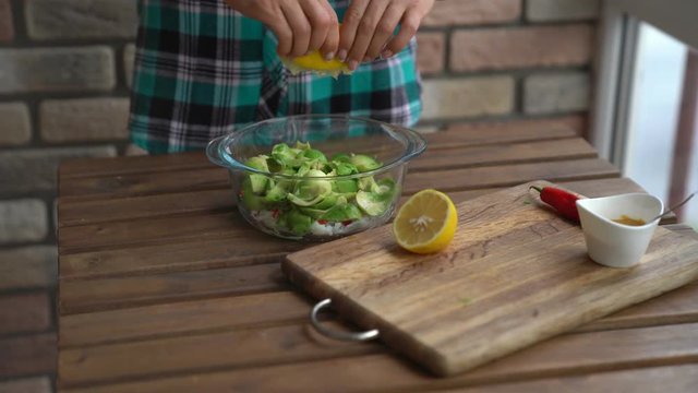 Closeup of female hands squeezing half a lemon to avocado for guacamole at table in home kitchen