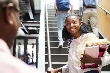 Female High School Student Talking With Teacher In Busy Corridor