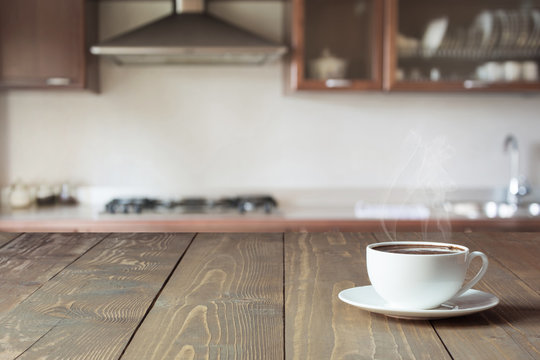 Cup of black coffee on wooden tabletop in blurred modern kitchen. Copy space. Indoor.