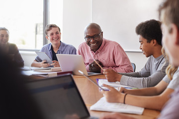 High School Teacher Talking To Pupils Using Digital Devices In Technology Class