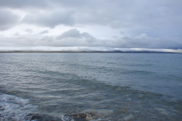 the highest lake in the world, sacred Namtso (Tibet), cold summer morning; light waves, low thunderclouds, snow-covered mountains in the distance