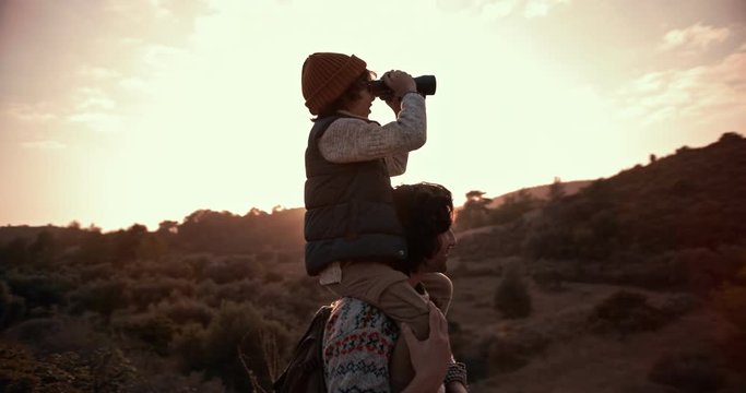Boy on father's shoulders using binoculars and looking at view