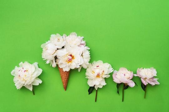 Ice cream cone with white peony flowers around on green background. Summer concept. Copy space, top view
