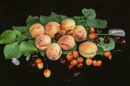 Large apricots and various types of cherries with green leaves on a black background
