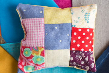 patchwork, quilting, sewing, tailoring and fashion concept - close-up beautiful colorful stitched cushion, macro on pillow with background of blue, gray and sand flaps of fabric, flat lay, top view.