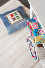 patchwork, sewing and fashion concept - two colorful quilted blankets at white shelves with few storage compartments in studio, pillow on floor in warehouse of finished products, top view, vertical.