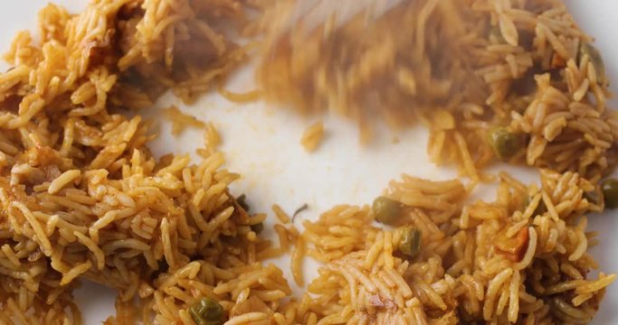 Close video of using a fork to separate steaming hot spicy rice on a white plate.