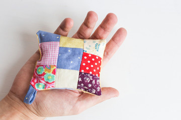 patchwork, quilting, sewing, tailoring and fashion concept - close-up on beautiful colorful stitched pincushion in human hand, macro on pillow with white background, flat lay, top view.