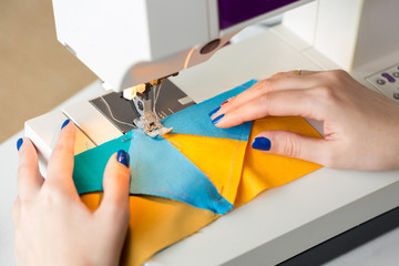 equipment, clothing, hobby concept. there is a close up of delicate arms of dressmaker who is working at the table with help of sewing machine, she is stitching few pieces of fabric