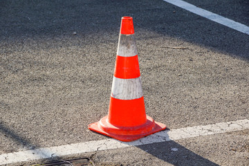 traffic cone, with white and orange stripes on gray asphalt,