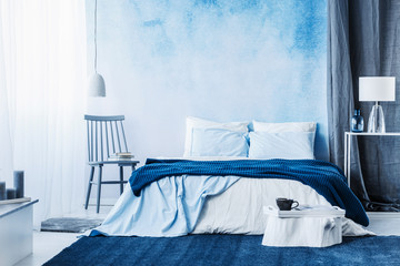 Navy blue carpet in minimal bedroom interior with blanket on bed next to a chair and under a lamp