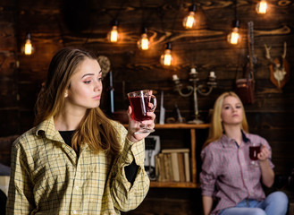Friends on relaxed faces in plaid clothes relaxing, defocused. Friends enjoy mulled wine in warm atmosphere, wooden interior. Rest and relax concept. Girls relaxing and drinking mulled wine