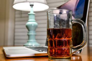 A beverage in a clear glass mug sit on an at home work station with a laptop and a lamp next to it.