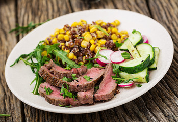 Healthy dinner. Bowl lunch with grilled beef steak and quinoa, corn, cucumber, radish and arugula on wooden background. Meat salad.
