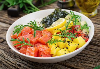 Hawaiian salmon fish poke bowl with rice, avocado, mango, tomato, sesame seeds and seaweeds. Buddha bowl. Diet food.