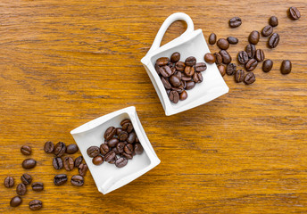 Coffee cup broken in two halves on wooden surface with coffee beans splashing out of them. Flat lay view.
