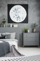 Moon poster above grey cabinet and bed in modern bedroom interior with plants. Real photo