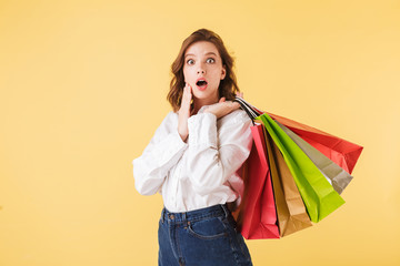 Portrait of young lady in shirt and denim shorts standing with colorful shopping bags in hands and...