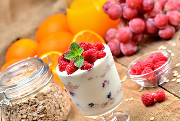 Yogurt, fresh raspberries in a glass and mint leaves, oranges, grapes and full glass of oatmeals in background - healthy breakfast concept