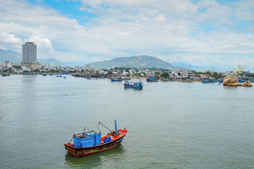 Fototapeta premium fishing schooners in the parking lot, in the riverbed of the Kai River, on the background buildings, mountains, and the sky covered with clouds, Nha Trang, Vietnam