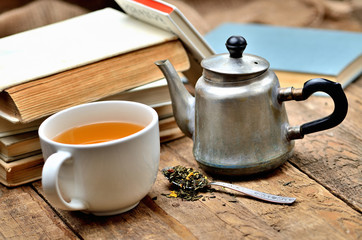 Detail of stack of old books, black tea, old teapot and spoon with tea loose and blue book in...