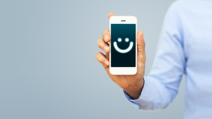 Hand of client show a feedback with smiley face card on smart phone. Service rating, satisfaction, customer experience concept