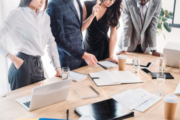 partial view of multiracial group of business coworkers in formal wear discussing new business plan in office
