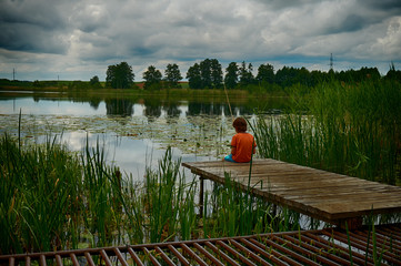 Fototapeta na wymiar Alone child sitting on the edge of a wooden pier