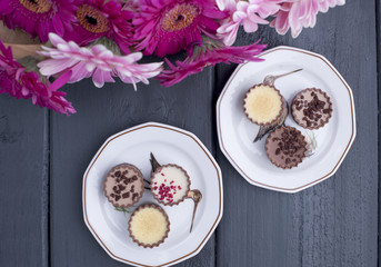 Different beautiful chocolate, on plates, a bouquet of fresh flowers. Black wooden background, free space for text. Copy space, flat lay.
