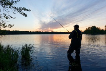 Silhouette of fisherman standing in the lake and catching the fish during sunrise
