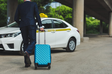 back view of young man with suitcase running to taxi cab