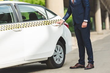 cropped shot of young man in suit opening door of taxi cab