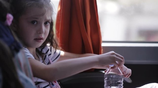 A little girl travelling in bus and drinks water from a plastic bottle