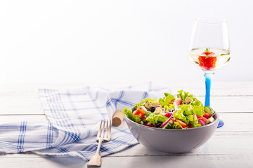 Fresh greek salad served in bowl with glass of white wine.