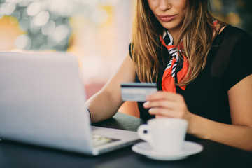 Fototapeta premium Happy young woman using credit card and laptop for shopping while sitting in cafe.
