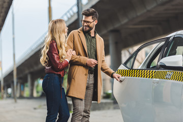 happy stylish young couple smiling each other while opening door of taxi car