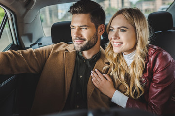 smiling young couple looking at car window while sitting together in taxi