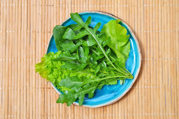 Summer green vegetables arugula salad spinach in blue plate on wooden surface top view