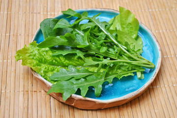 Summer green vegetables salad spinach arugula in blue plate on wooden surface
