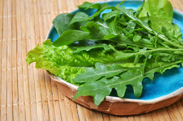 Summer green vegetables salad arugula spinach in blue plate on wooden surface